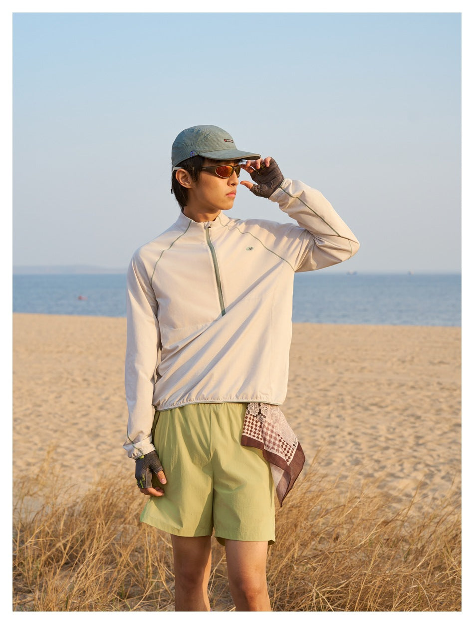 Closer view of a man wearing a cream quarter-zip top and olive shorts on a beach.