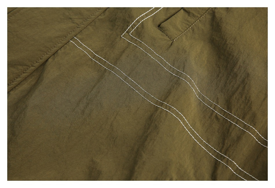 Close-up of olive-brown fabric with parallel white topstitching and a small pocket opening.