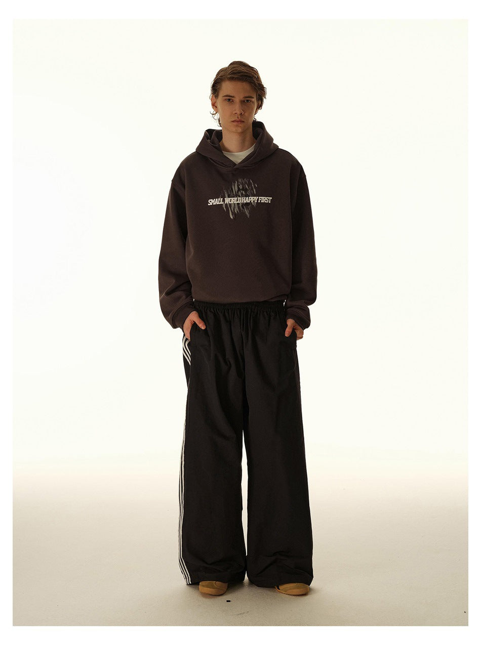 Model wearing a dark brown graphic hoodie and loose black track pants with light side stripes.