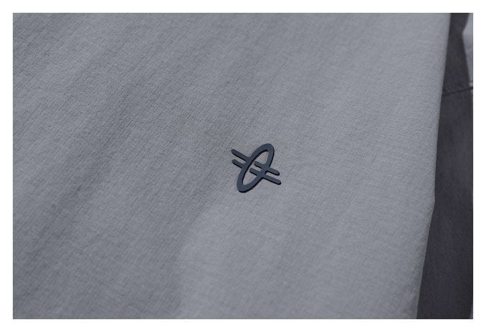 Close-up of a small dark emblem on gray fabric with a subtle grid texture.