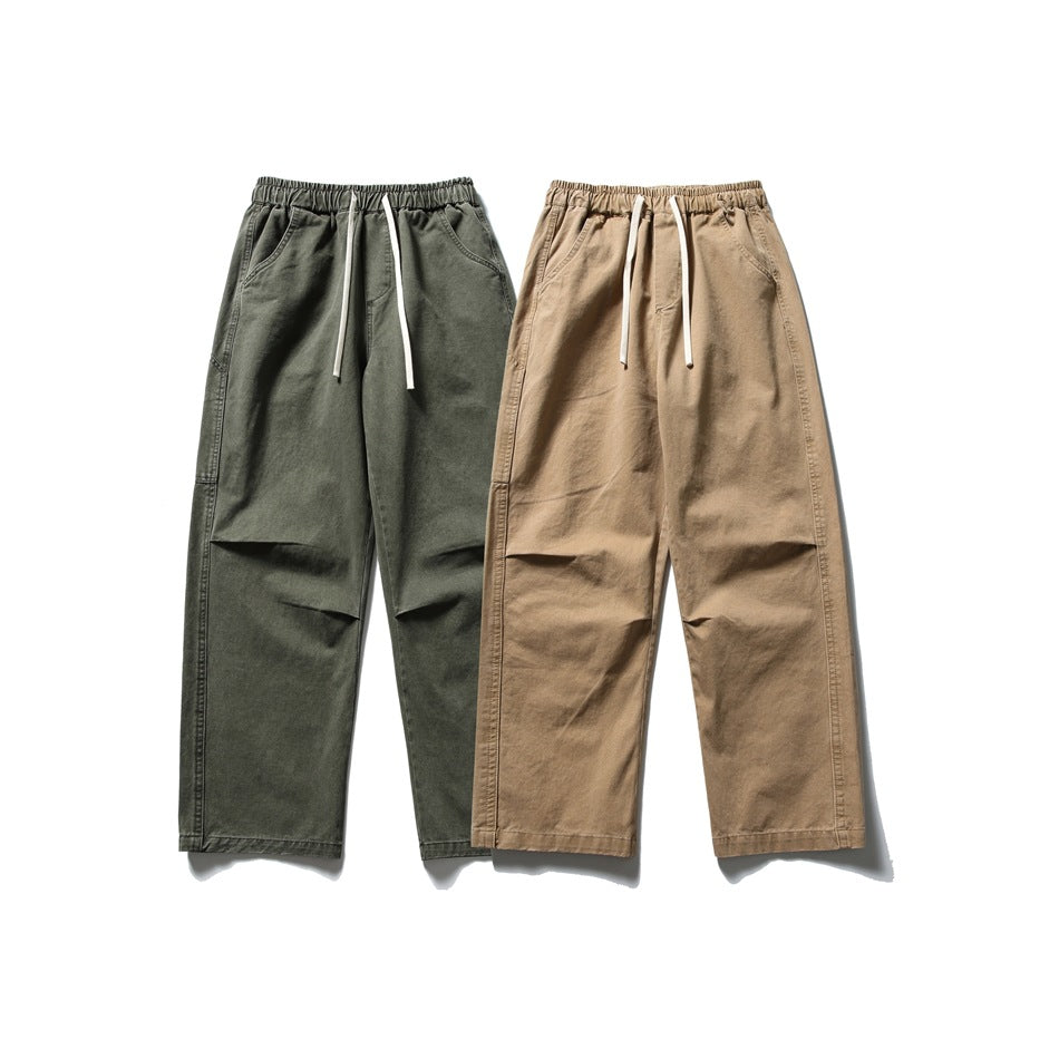 Two pairs of relaxed straight-leg trousers shown from the front in dark olive and tan, with elastic waists and drawstrings.