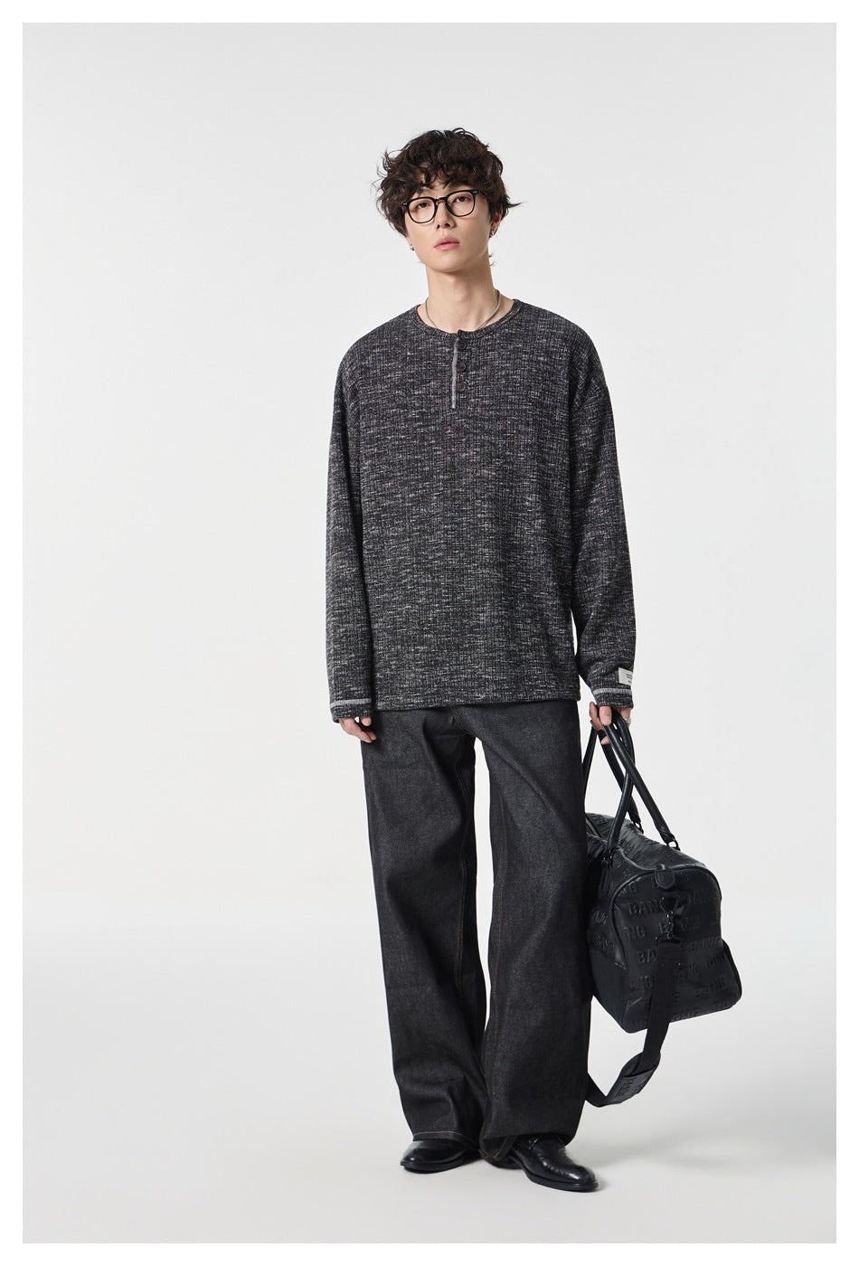 Full-length model wearing a charcoal marled Henley and dark wide-leg trousers, carrying a black duffel bag.