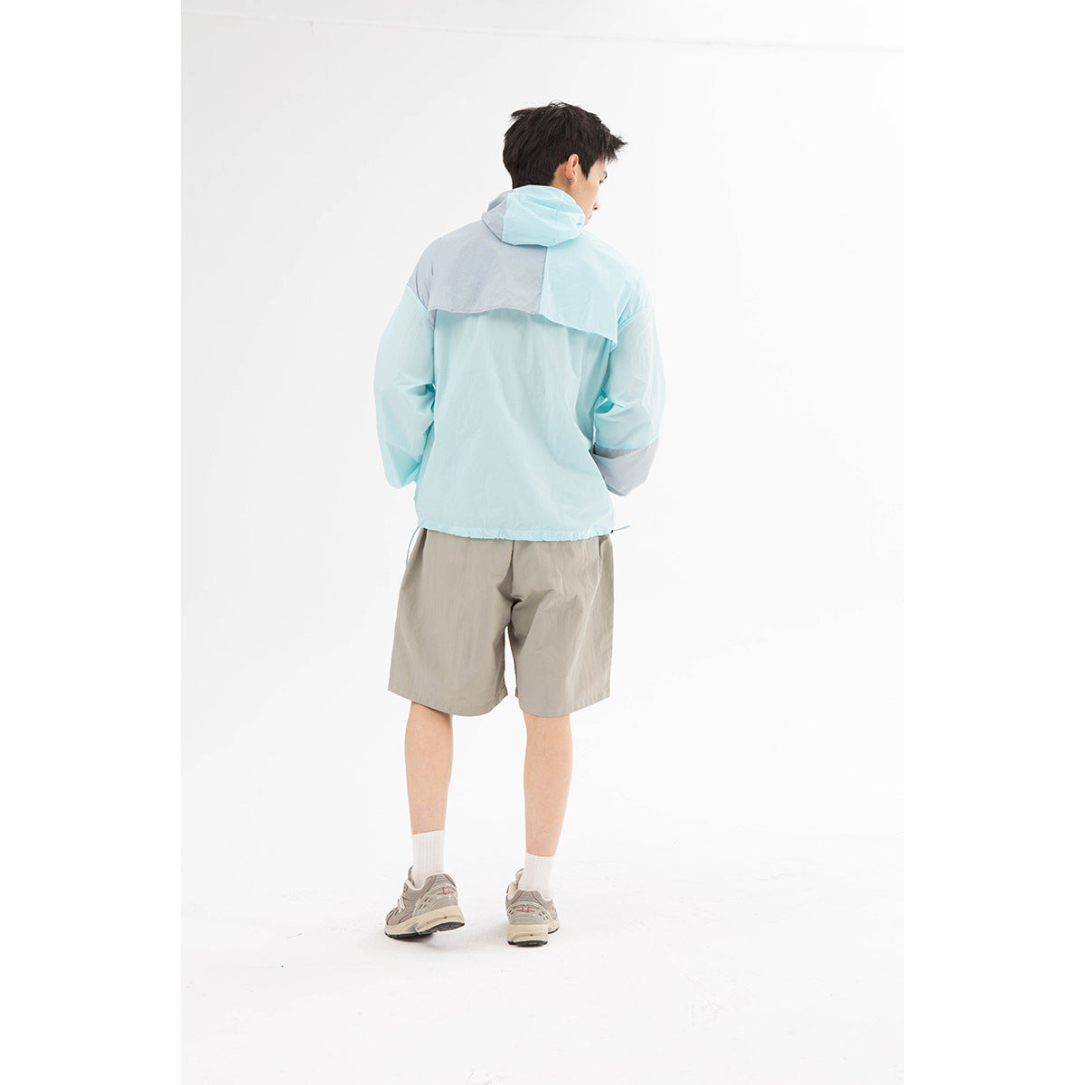 Back view of a model wearing a pale aqua color-block hooded jacket and taupe shorts.