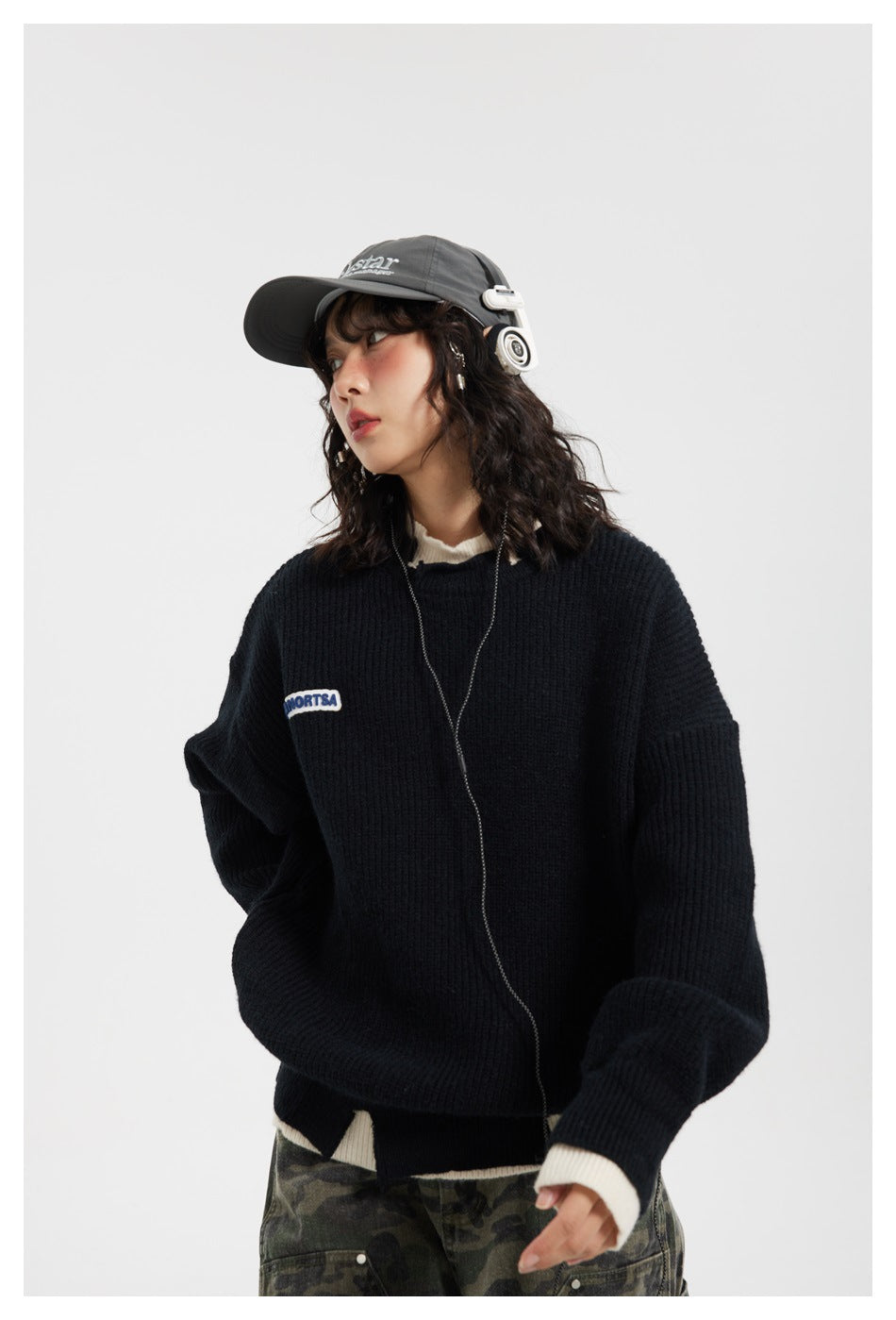 Three-quarter view of a model in an oversized black ribbed sweater with cream trim and camouflage pants.