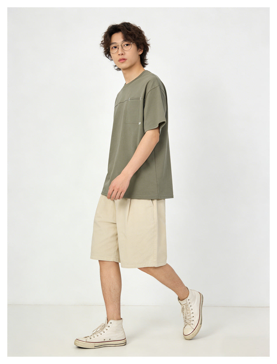 Model walking in an olive green oversized T-shirt with chest pocket, side view, with beige shorts and sneakers