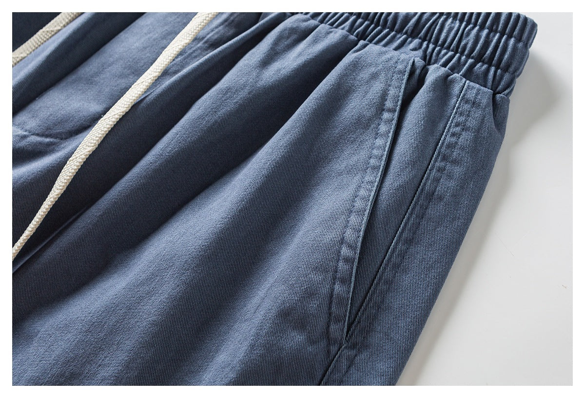 Close-up of blue pants showing a front pocket, gathered waistband, and cream drawstring.