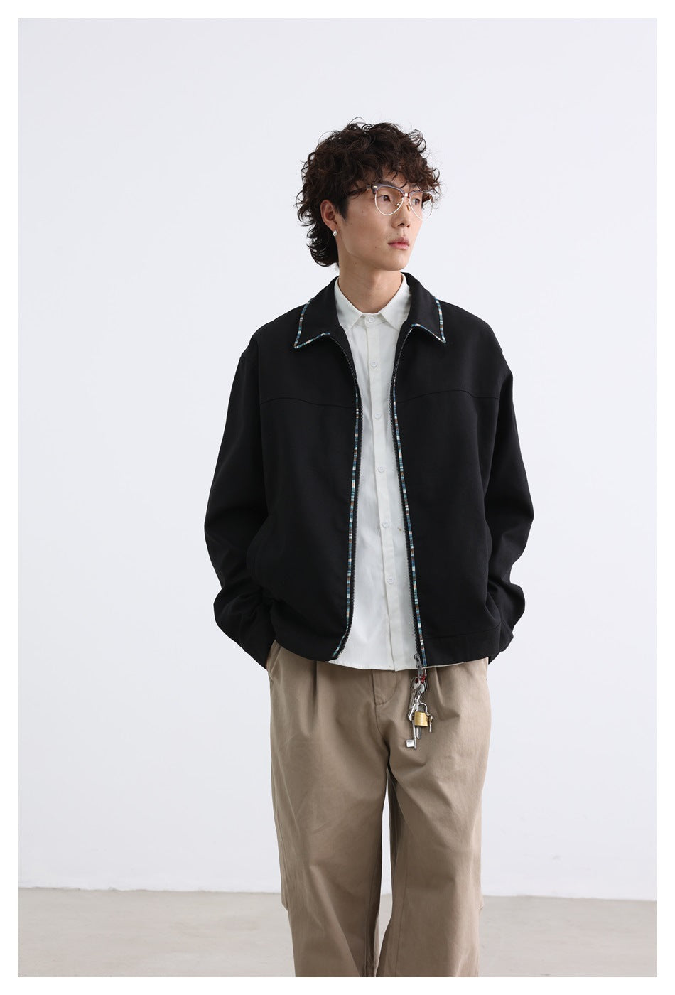 Front view of a model in a black zip-front jacket with multicolor trim, white shirt, and beige trousers.