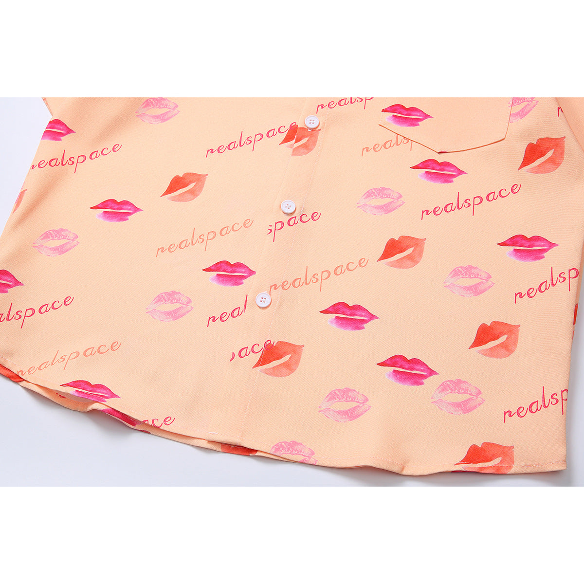 Close-up of the peach shirt's lower front, showing buttons, hem, and repeating pink lip print.