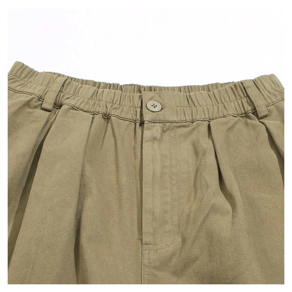Close-up of khaki trousers showing the elastic waistband, button, belt loops and front pleats.