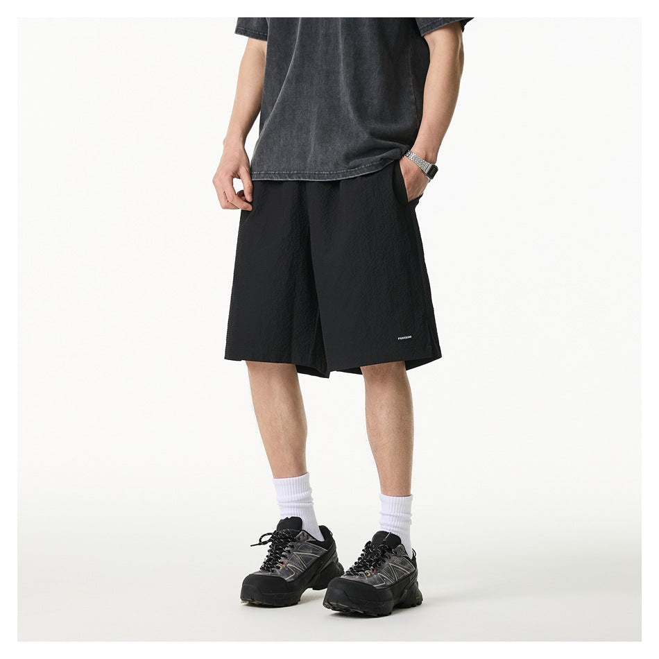 Model wearing black textured knee-length shorts with a faded gray tee, white socks and black sneakers