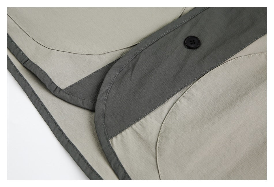 Close-up of light gray fabric with a dark curved button placket and visible stitching.