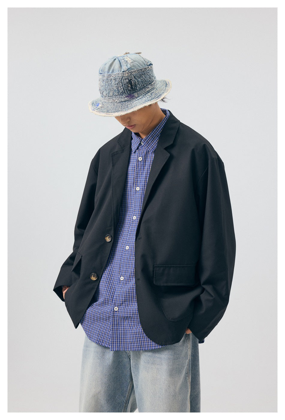 Close view of model in black blazer jacket over blue checked shirt, with distressed denim bucket hat