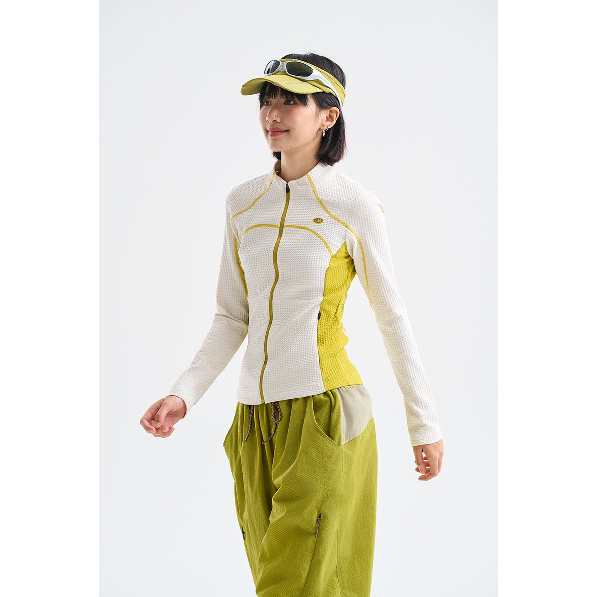 Model wearing a white zip-front jacket with yellow contrast panels and olive-green trousers.