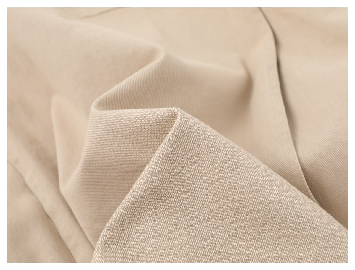 Close-up of light beige fabric folded to show its fine diagonal weave.
