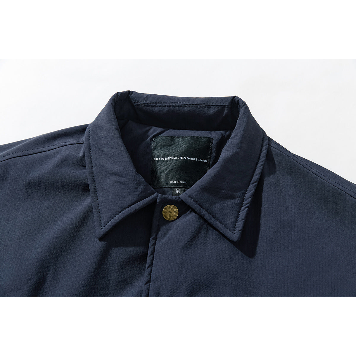 Close-up of a navy jacket collar, brass-tone snap, and sewn-in neck label.