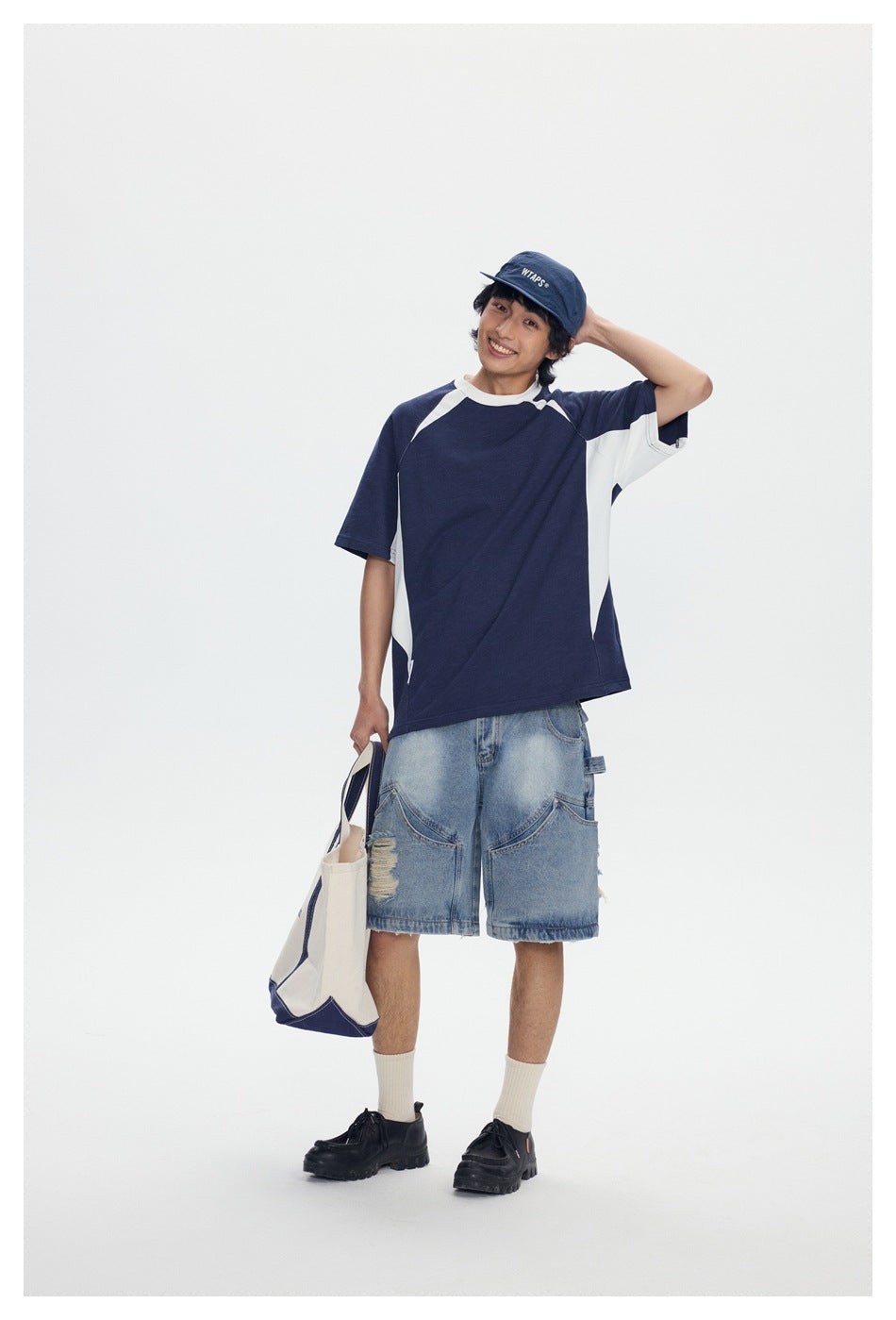 Model wearing a navy and white raglan T-shirt with light-wash denim shorts, shown from the front.