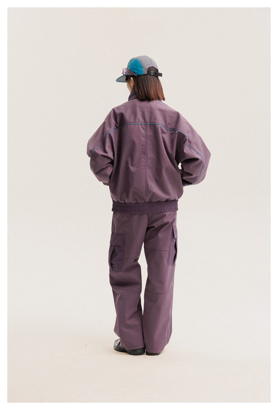 Back view of a model wearing a plum jacket with turquoise piping and matching cargo pants.