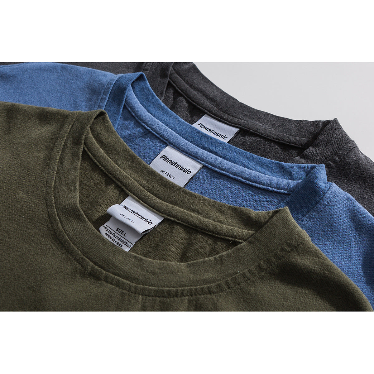 Close-up of olive, blue, and charcoal T-shirt collars with sewn neck labels.