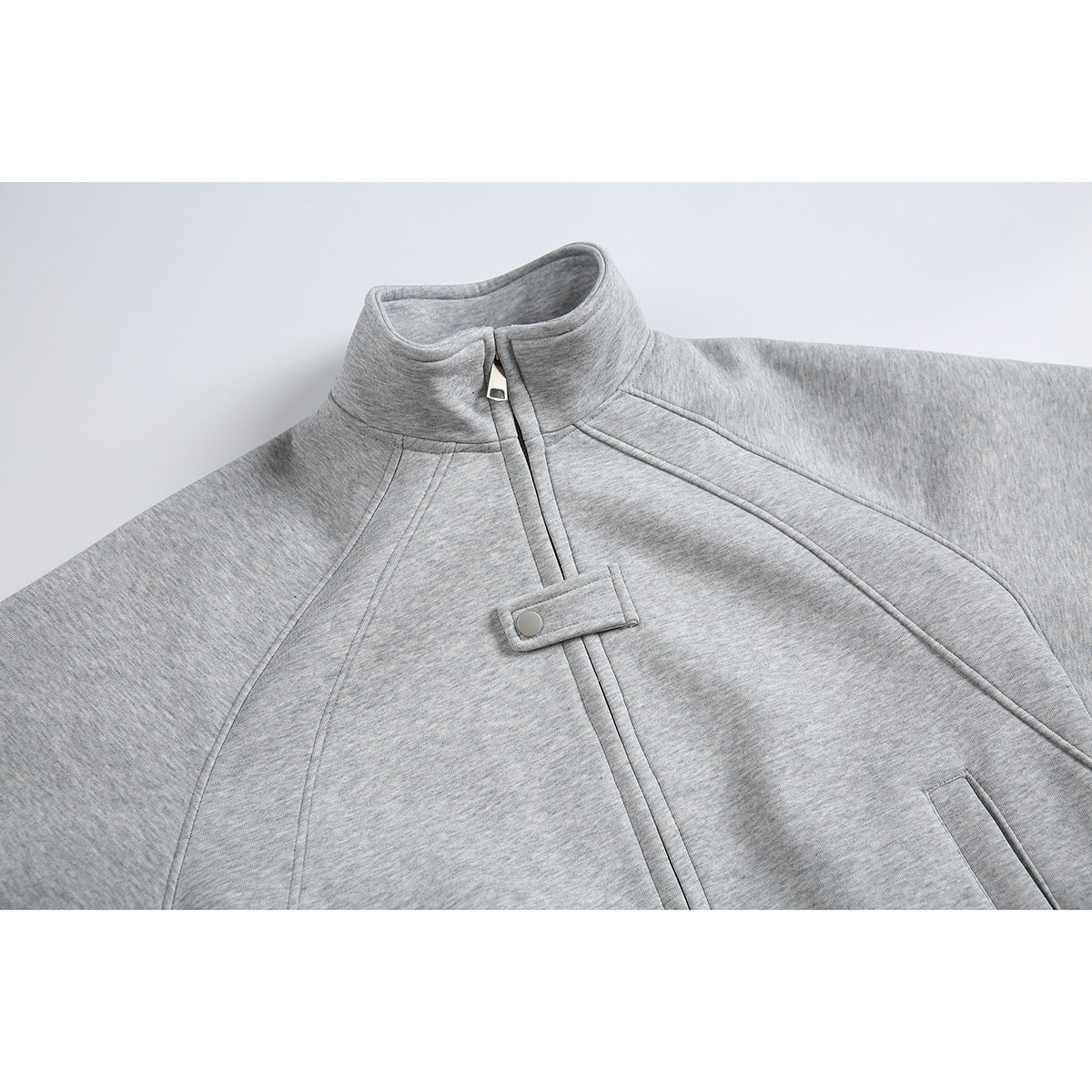 Close-up of a heather-gray jacket showing its stand collar, front zipper, snap tab, curved seams, and pocket opening.