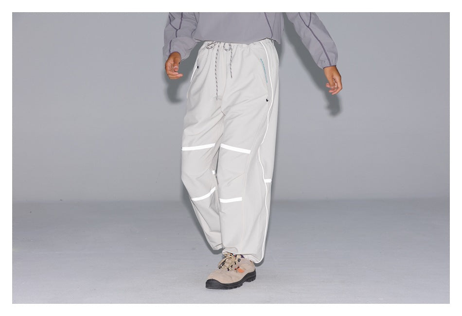 Front view of a person wearing light-gray drawstring pants with bright reflective bands across the legs.
