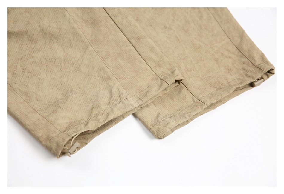 Close-up of tan trouser leg hems with small adjustable drawcord toggles.