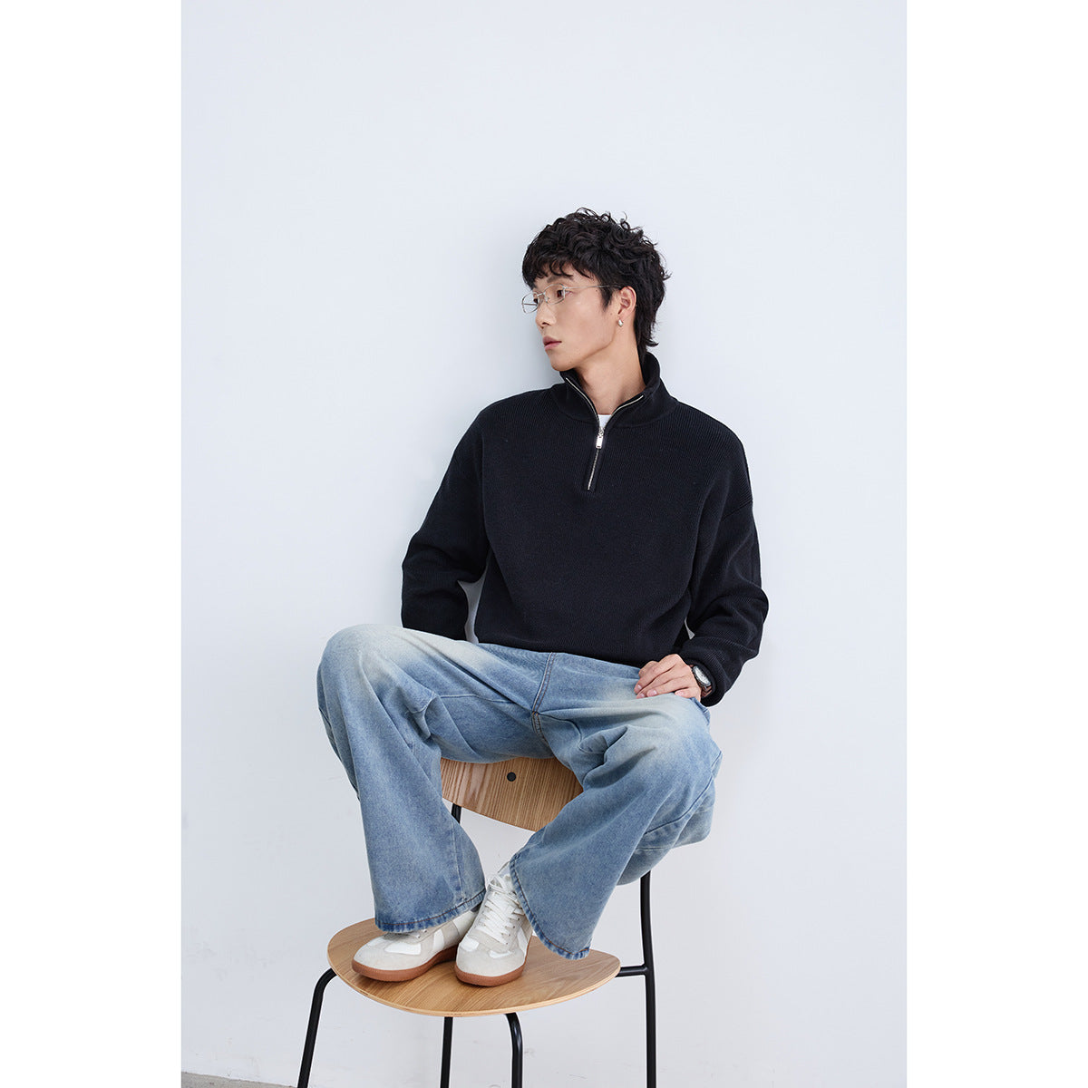 Seated model wearing a black high-collar quarter-zip pullover with light blue wide-leg jeans.