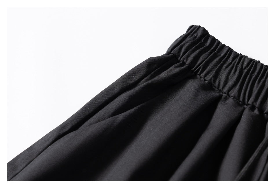 Close-up of black trousers showing the gathered elastic waistband and fabric folds.