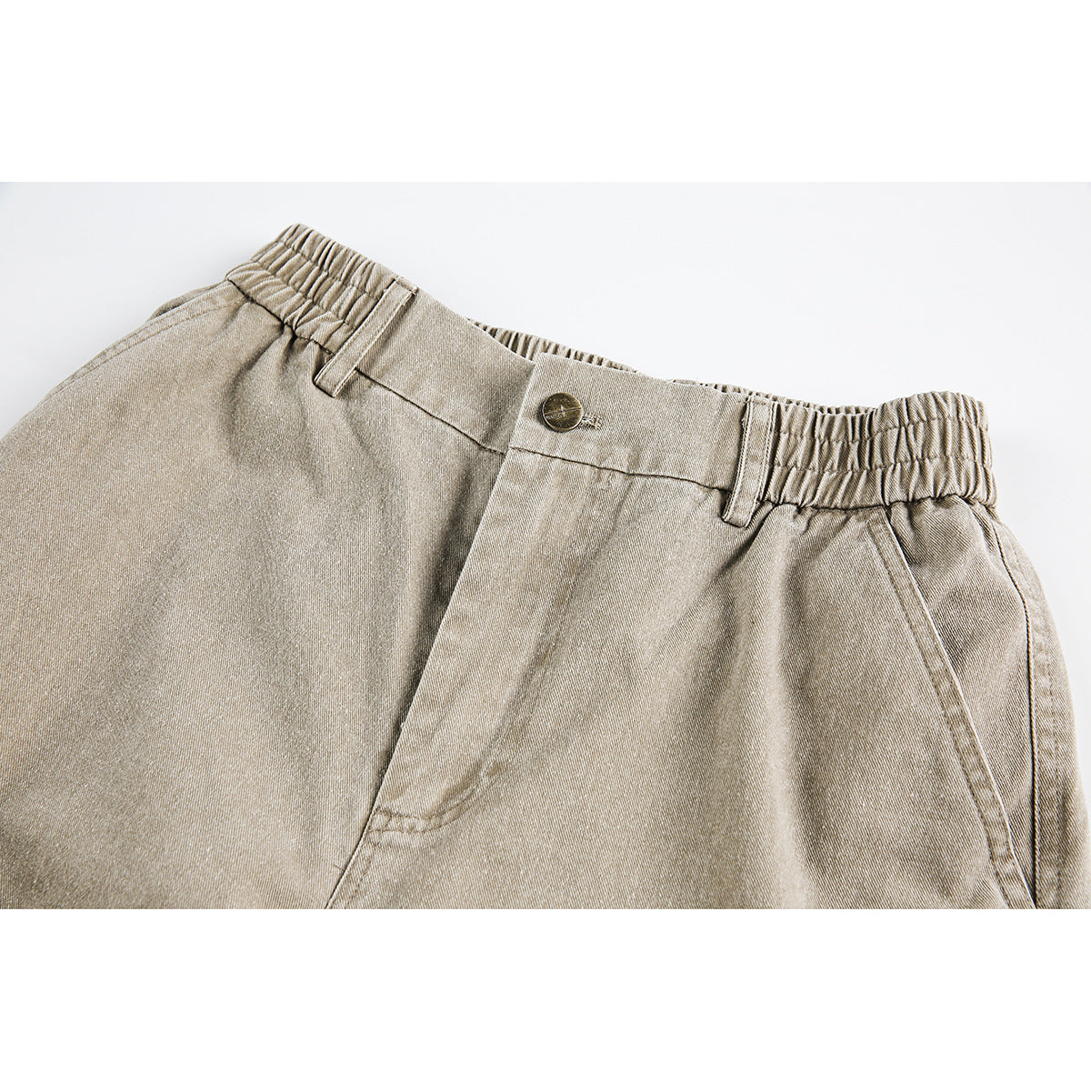 Close-up of light beige cargo pants showing an elasticized waistband, button, belt loops, and angled pocket seams.