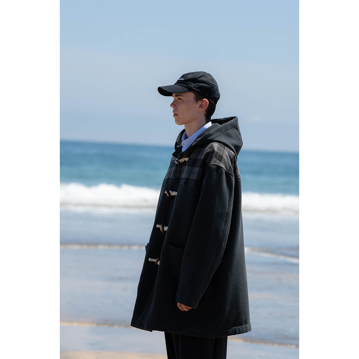 Side view of a person wearing a dark hooded duffle coat with plaid shoulder panels and toggle closures.