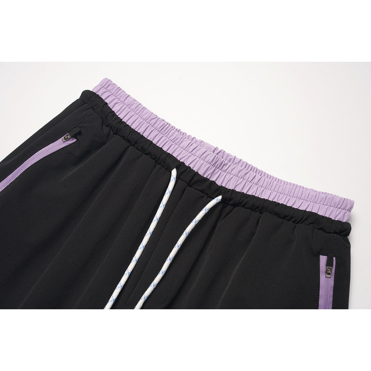 Close-up of black pants with a lavender elastic waistband and pocket trim, plus white drawstrings.