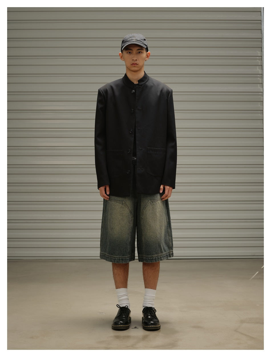 Front view of a model wearing a black band-collar button coat and oversized faded denim shorts with a gray cap.