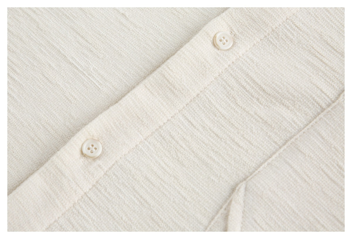 Close-up of two matching buttons on the placket of an ivory textured garment.