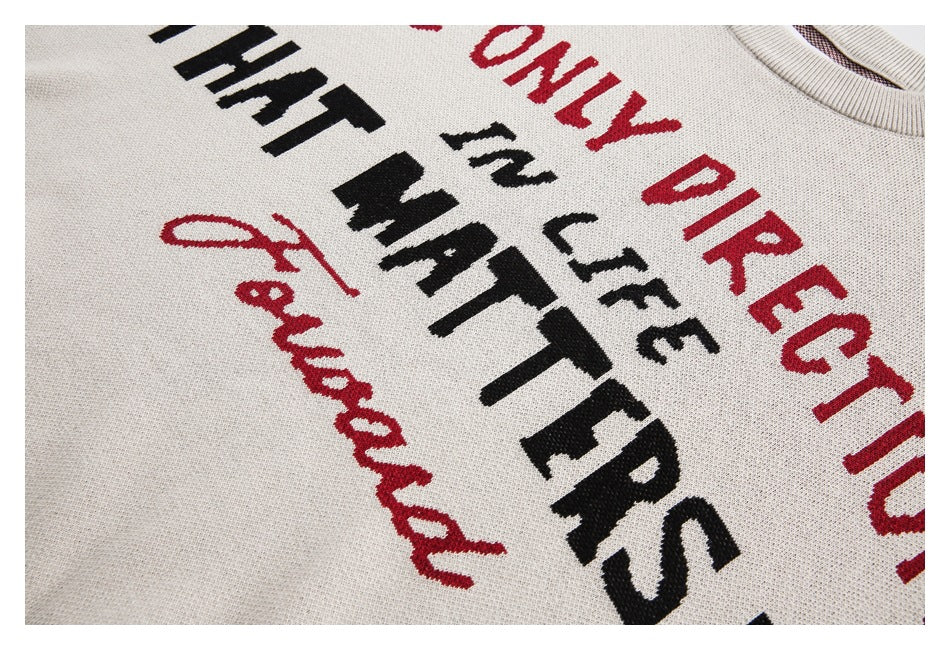 Close-up of a cream sweater with bold red and black English lettering knit into the front.