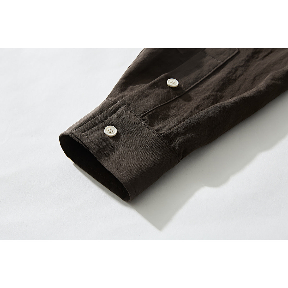 Close-up of a dark brown shirt sleeve and buttoned cuff on a white background.