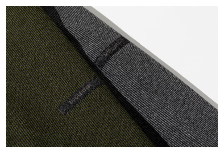 Close-up of olive and charcoal ribbed sweatshirt fabric with small black sewn-on labels.