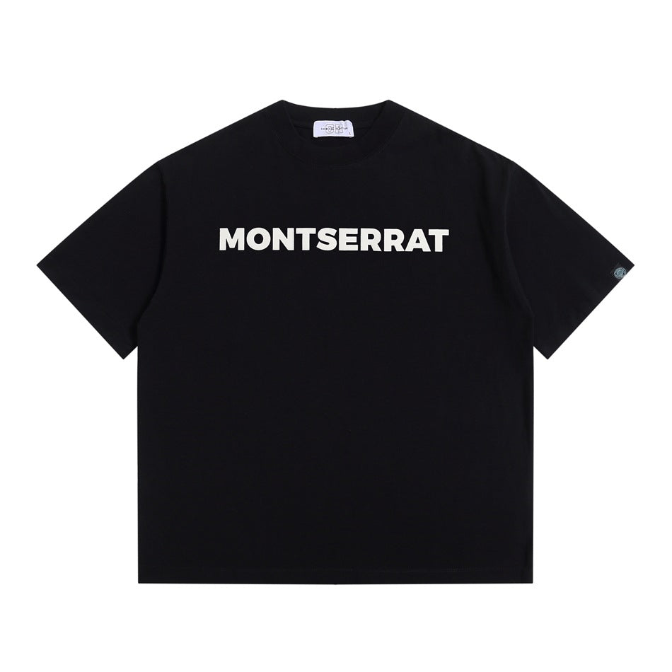 Black short-sleeve crewneck T-shirt with white MONTSERRAT block lettering on the chest, flat lay