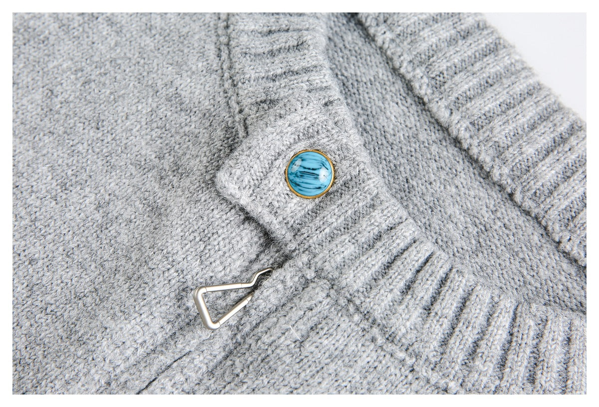 Close-up of a light gray knit sweater's blue button and triangular metal clasp at the ribbed neckline.