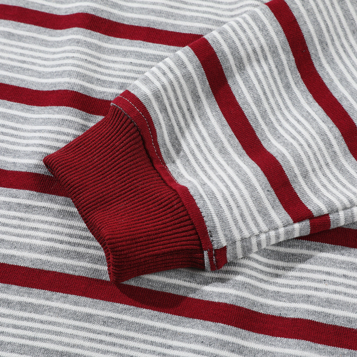 Close-up of a gray-and-white striped sleeve with a wide burgundy stripe and ribbed burgundy cuff.