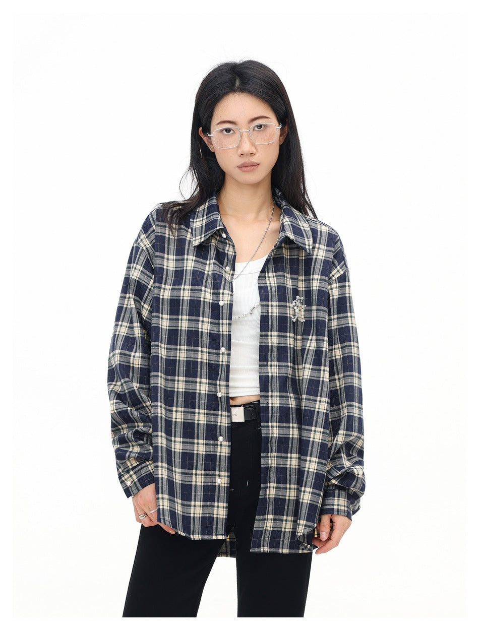 Model wearing an open navy and cream plaid shirt with pearl-like chest embellishment over a white crop top.