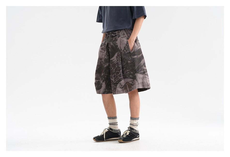 Side view of a person wearing wide-leg printed shorts with a hand in the pocket, navy tee and dark sneakers
