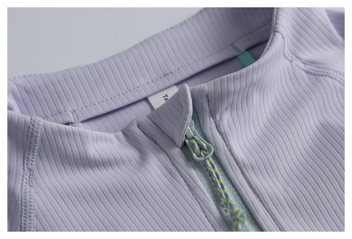 Close-up of a lavender ribbed garment’s high collar and front zipper with a patterned cord pull.