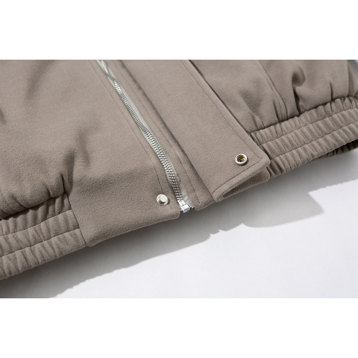 Close-up of the taupe jacket’s silver front zipper, snap placket, and gathered hem.
