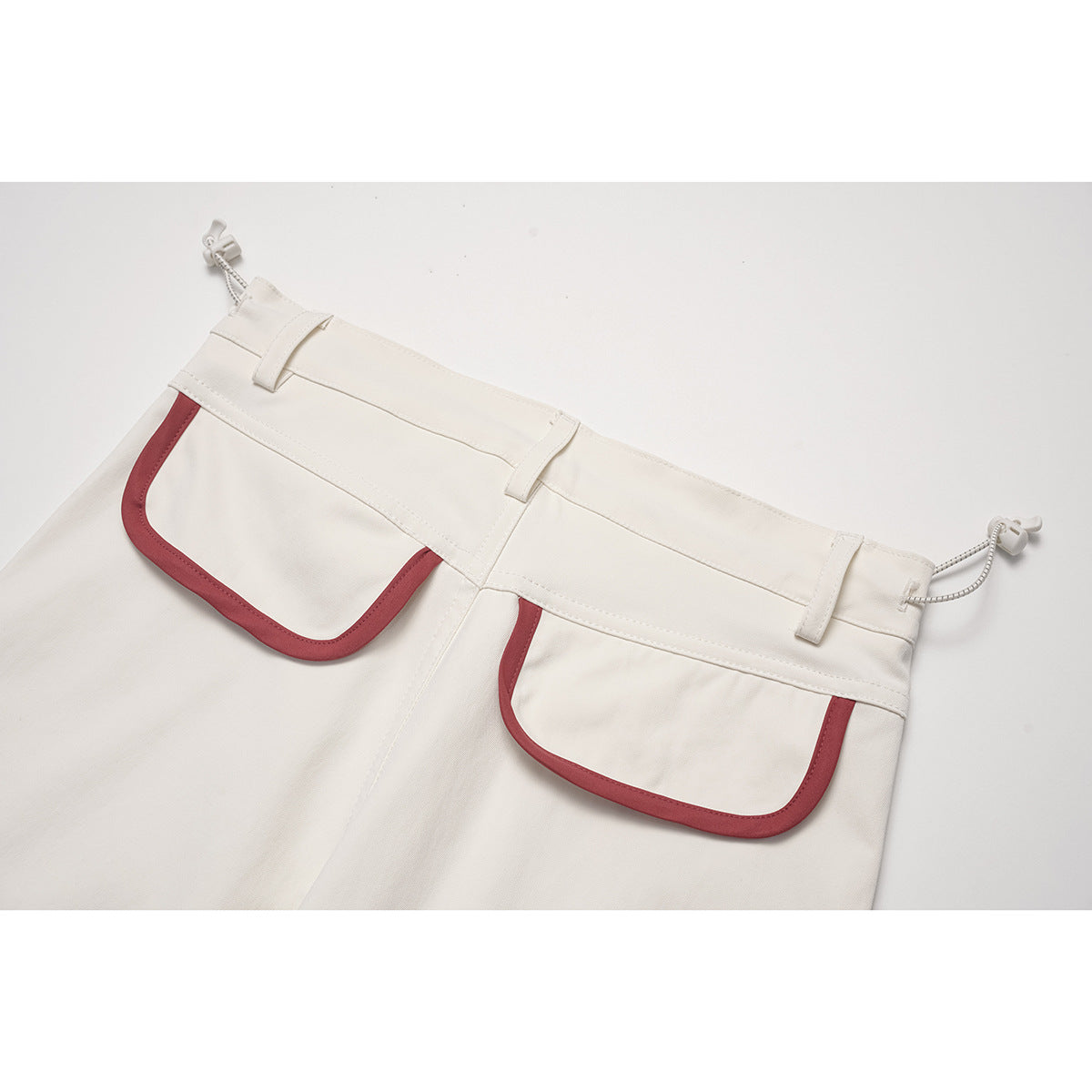 Close-up of the back waist and two large red-trimmed patch pockets on cream pants.