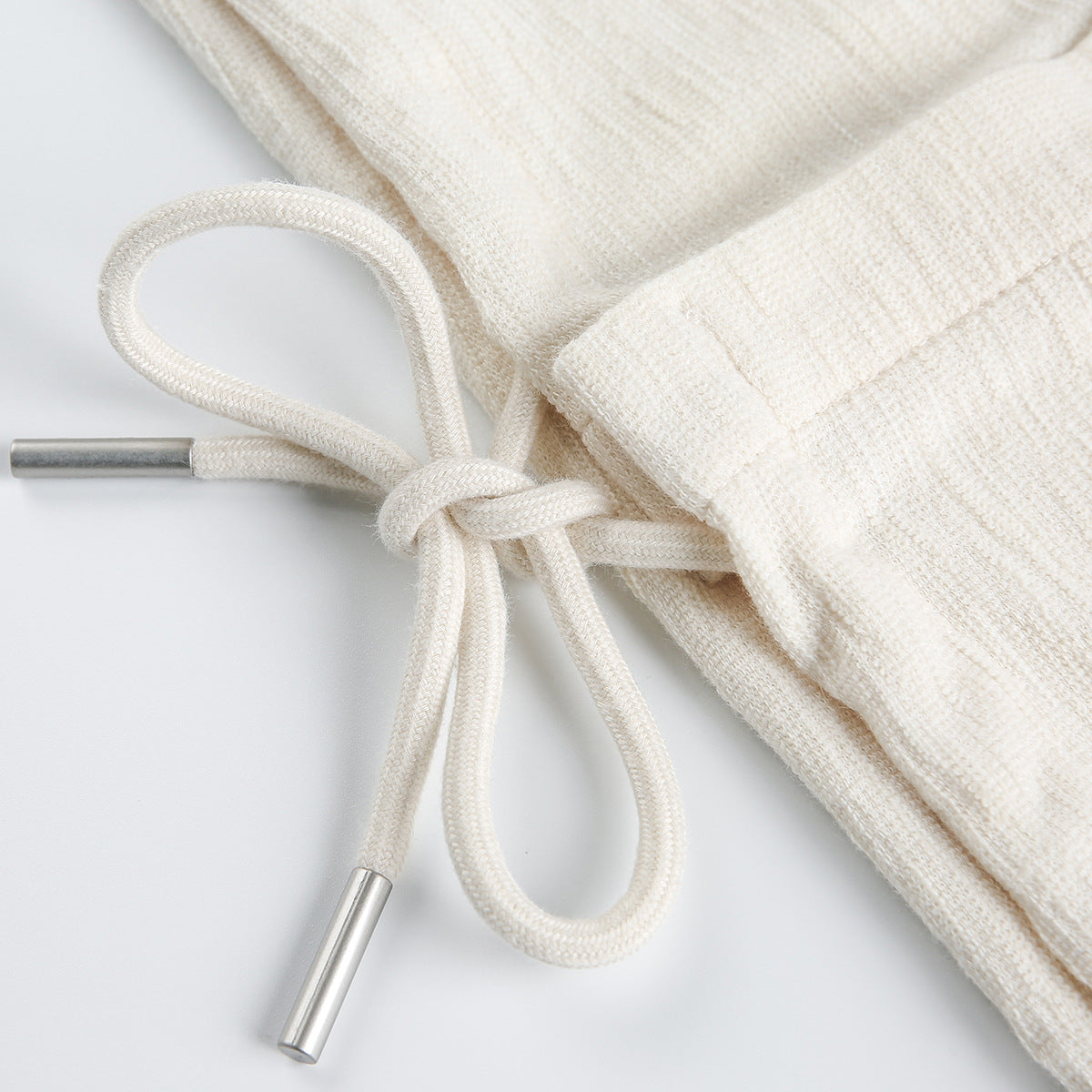 Close-up of a cream knit garment's drawstring waistband with metal-tipped cords.
