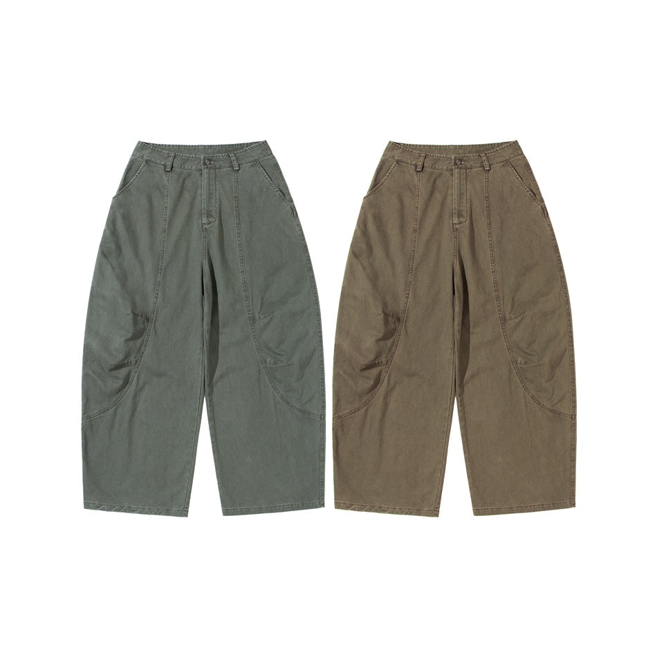 Front view of loose wide-leg pants in gray-green and muted brown, with curved panel seams and side pockets.