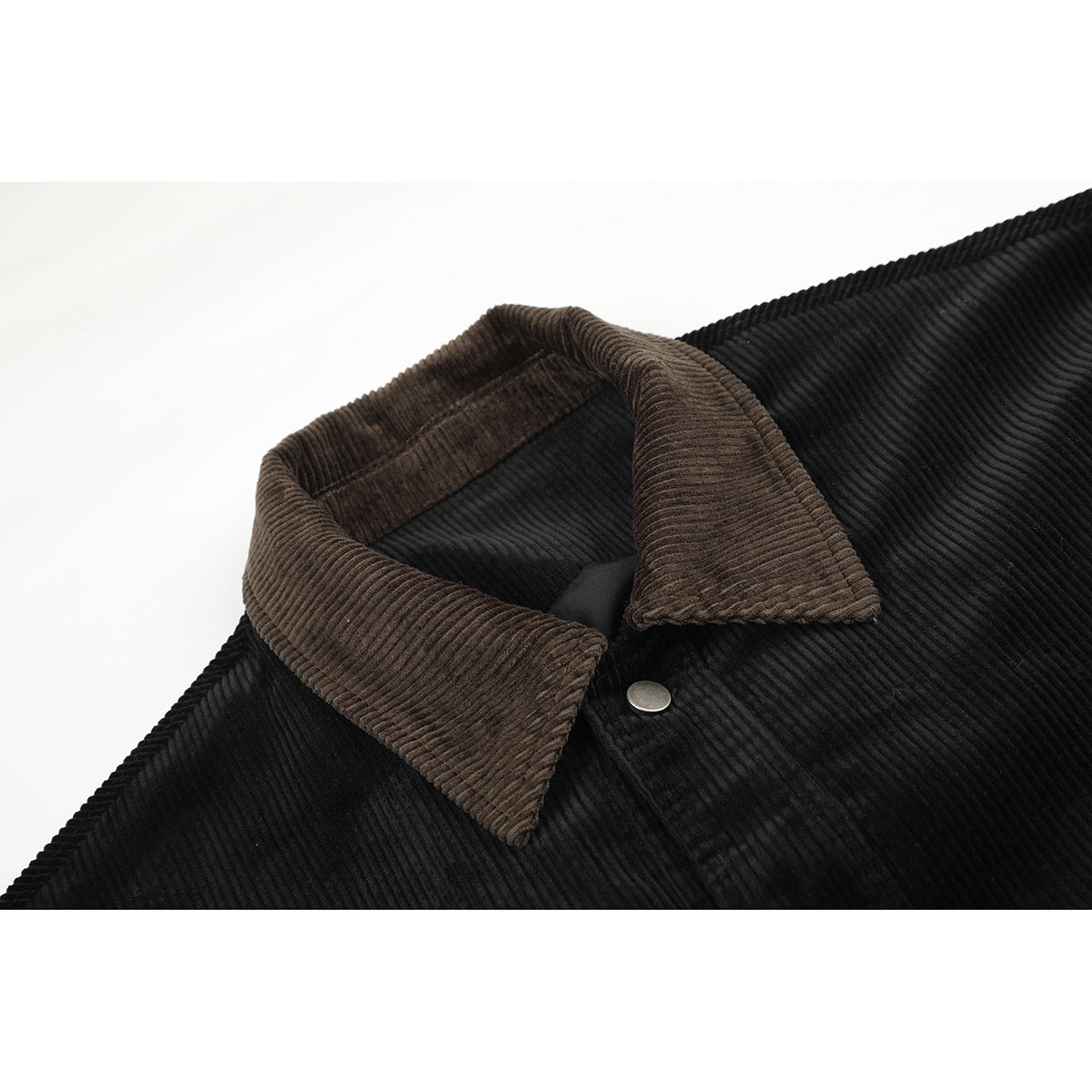 Close-up of a black ribbed jacket with a contrasting brown corduroy collar and silver snap.