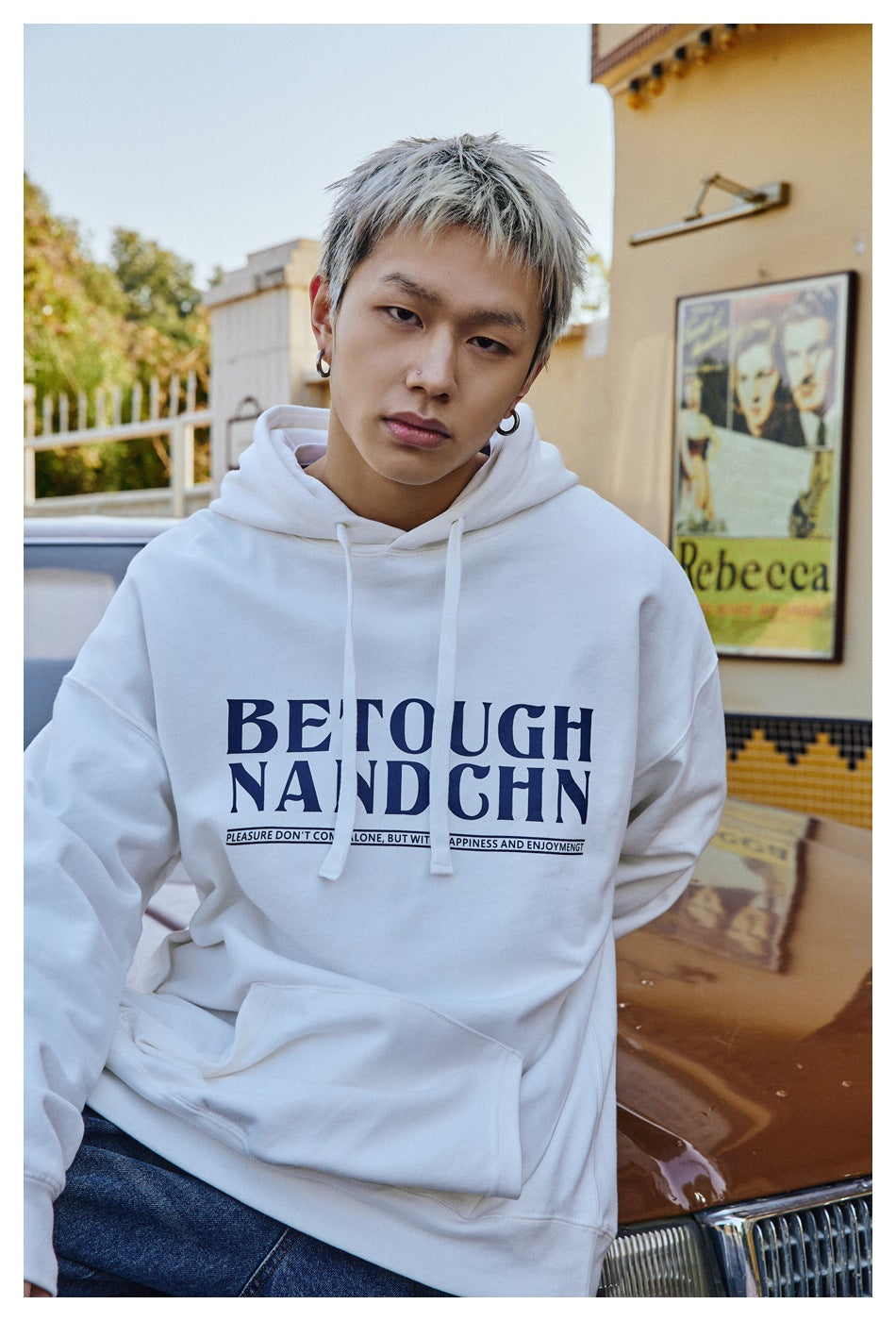 Close-up of a person in a white oversized hoodie with navy 'BETOUGH NANDCHN' print and drawstrings