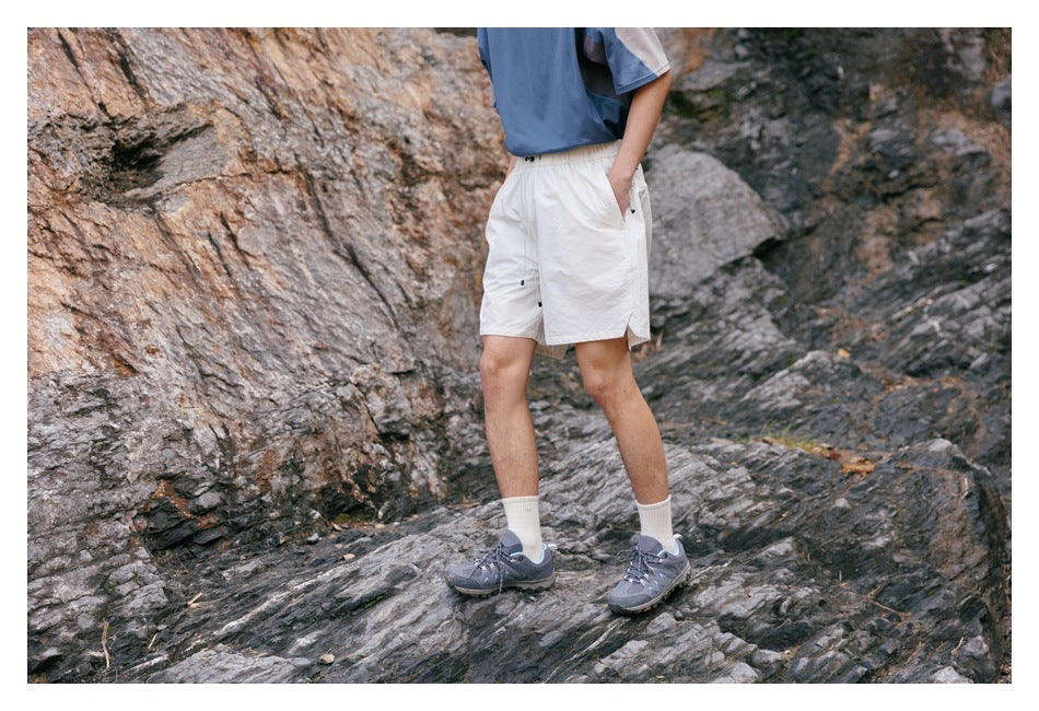 Cropped model standing on rocks in white elastic-waist shorts, shown at a slight angle.
