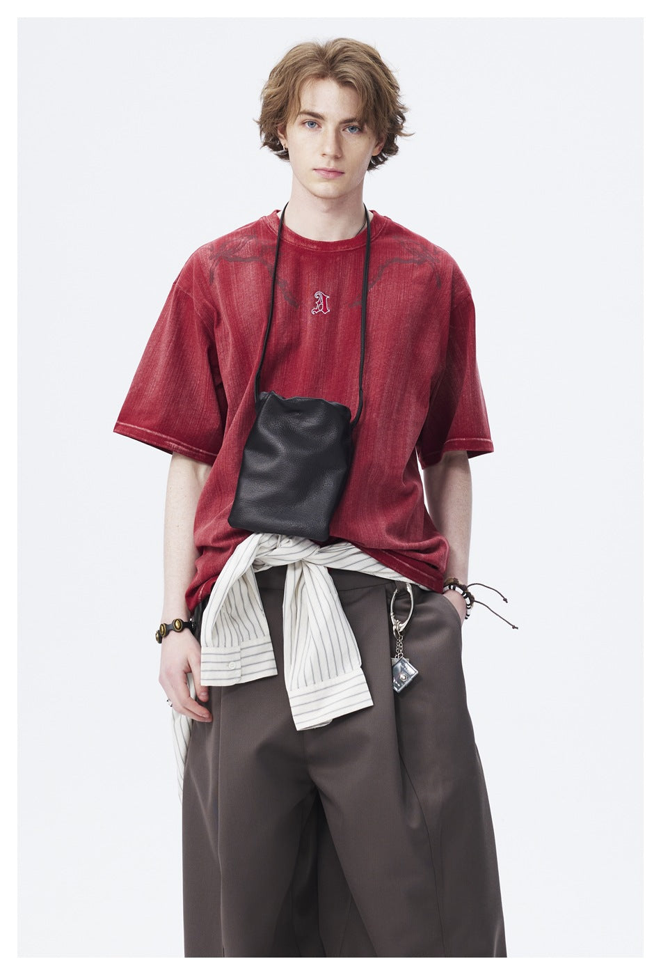 Closer view of a model wearing a faded red graphic T-shirt with a small chest emblem and dark trousers.