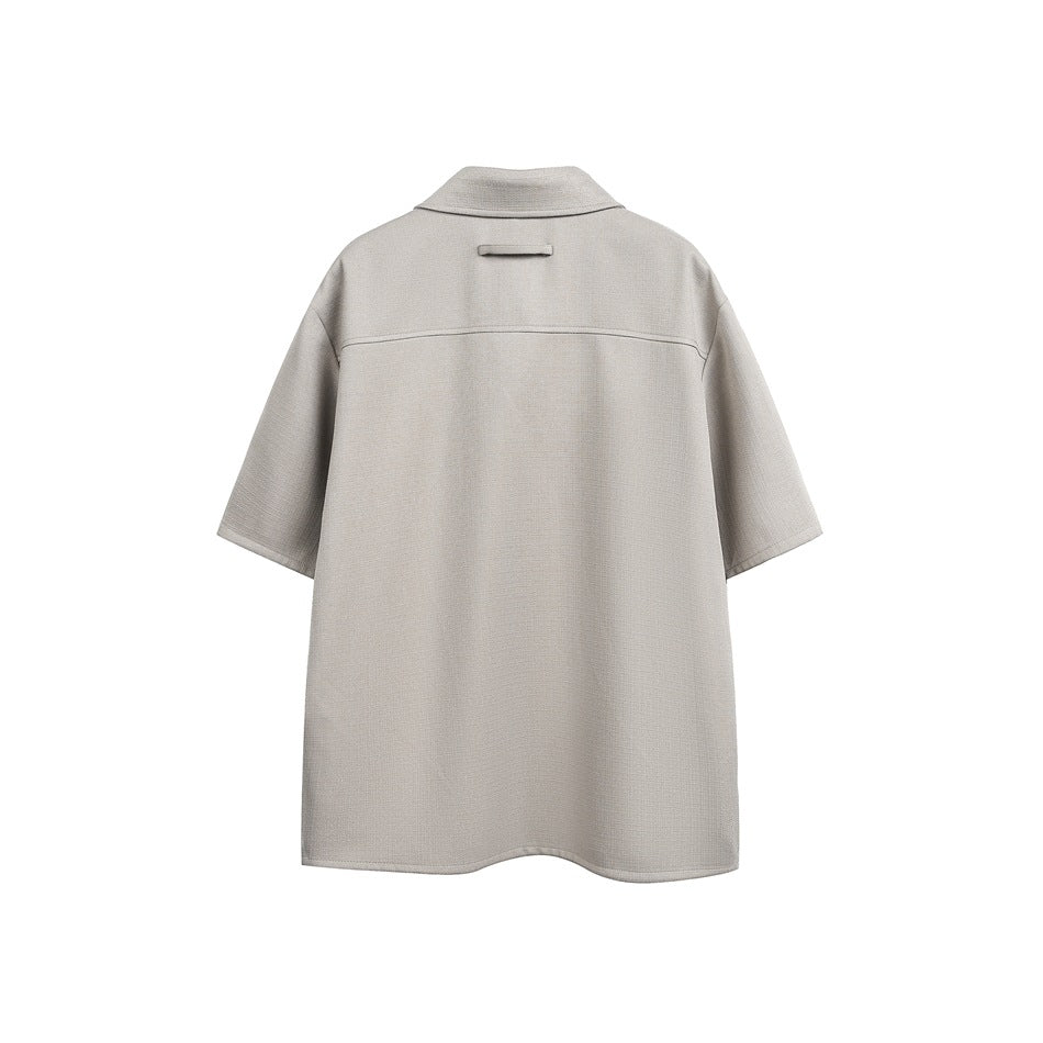 Back view of a light gray-beige short-sleeve collared shirt with a horizontal back yoke seam.